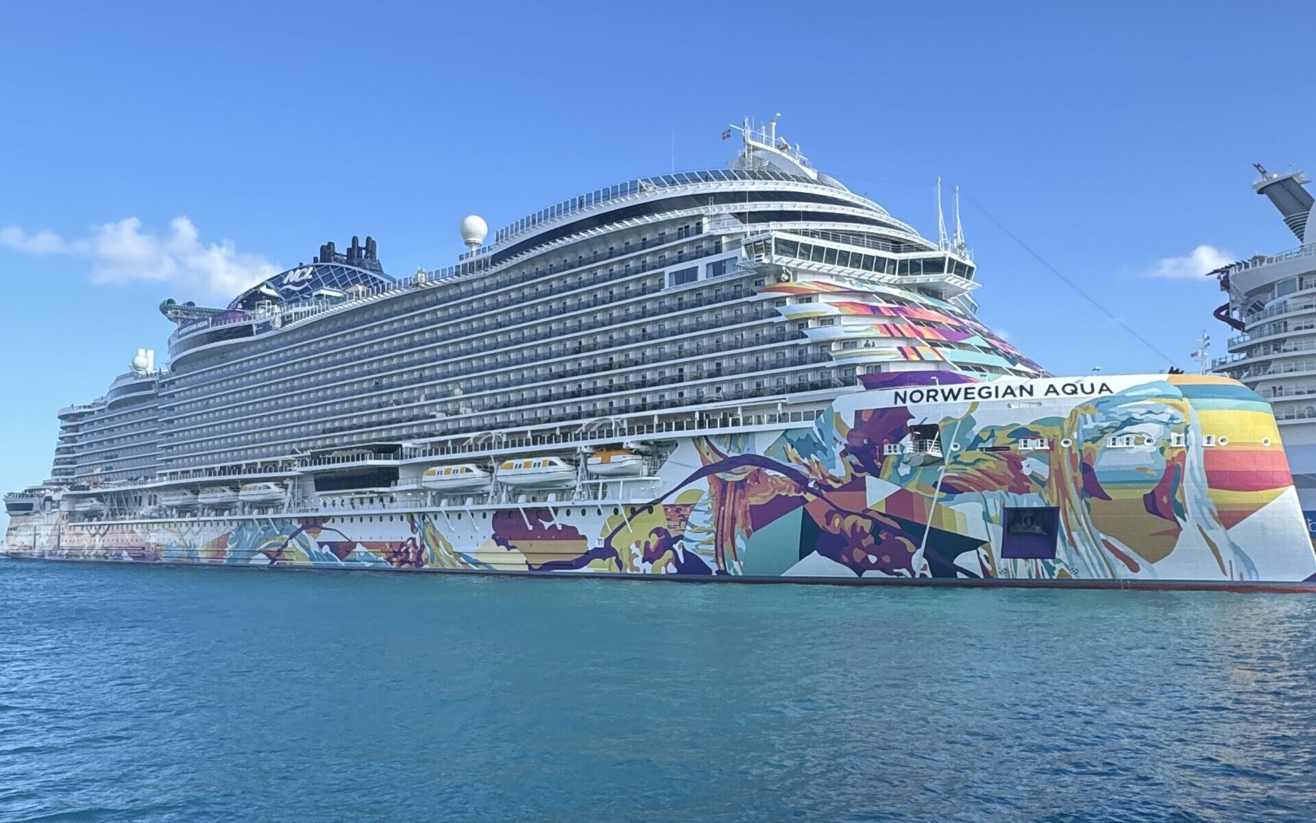 Exterior side profile of the Norwegian Aqua cruise ship docked in port, showcasing colorful hull art and upper passenger decks.
