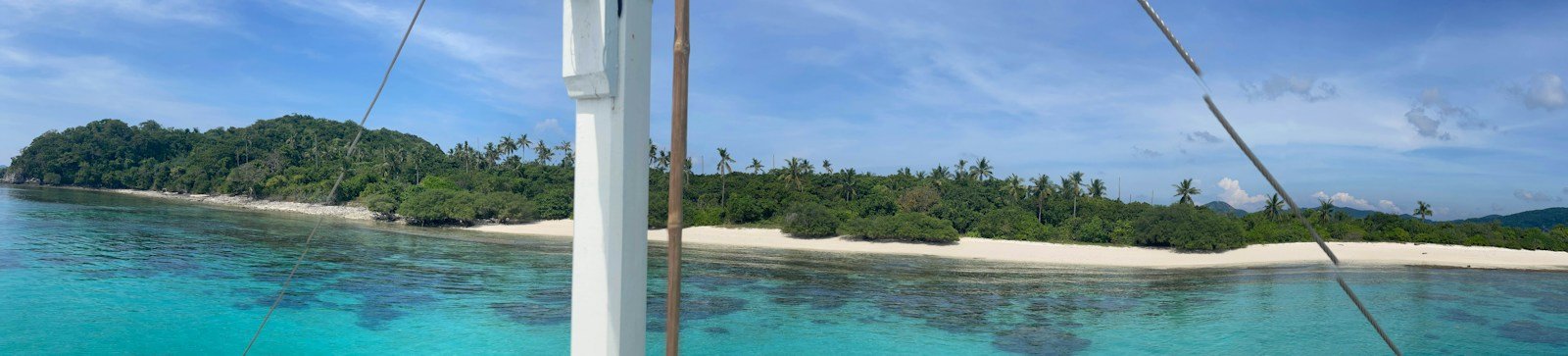 Panoramic view of a pristine white-sand beach and coconut palms accessed via yacht dinghy tender