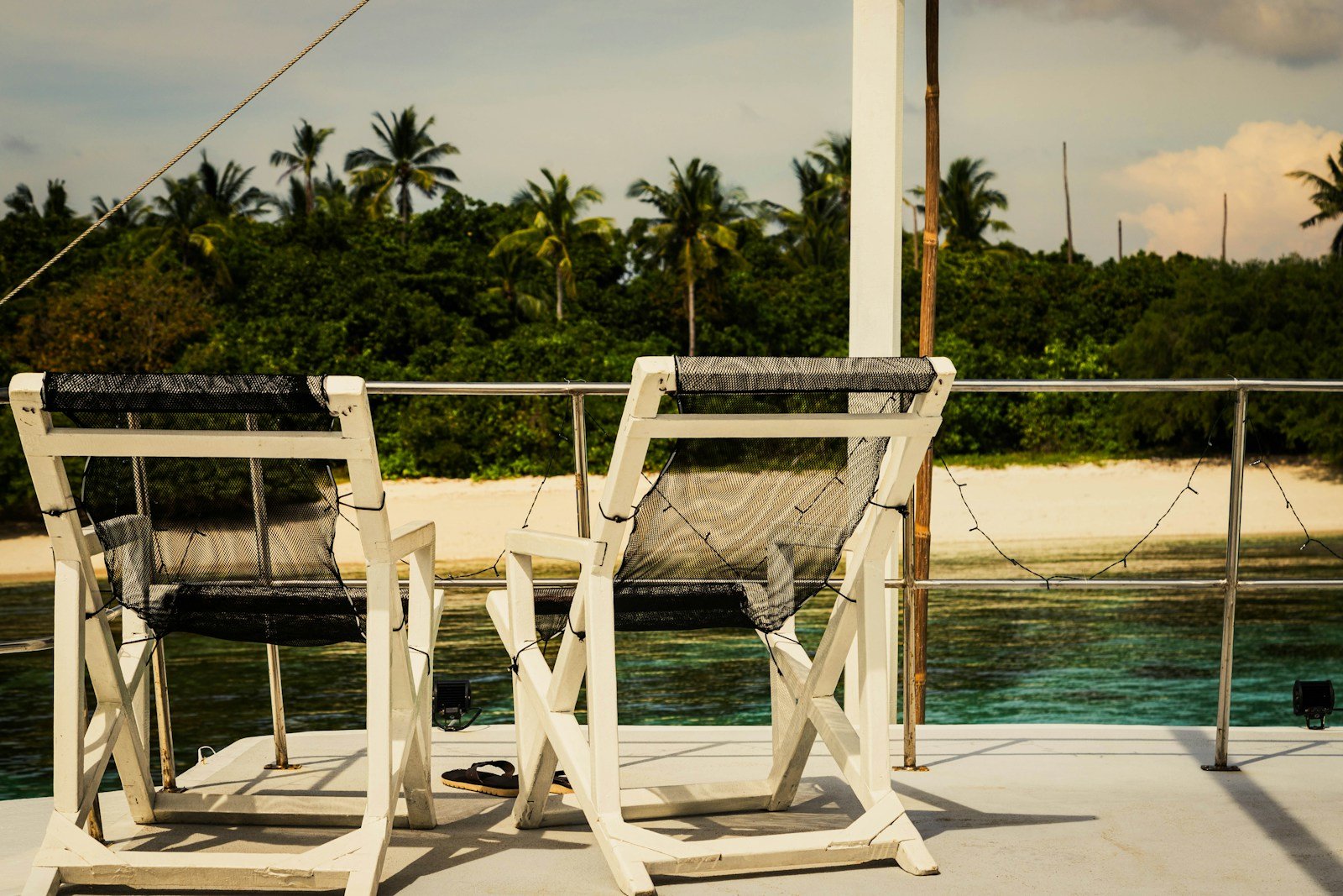 Comfortable deck chairs on an open flybridge yacht deck overlooking a pristine tropical beach