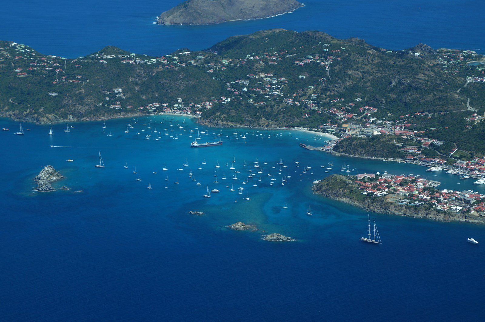 Aerial view of an emerald tropical island surrounded by coral reefs and anchored yachts