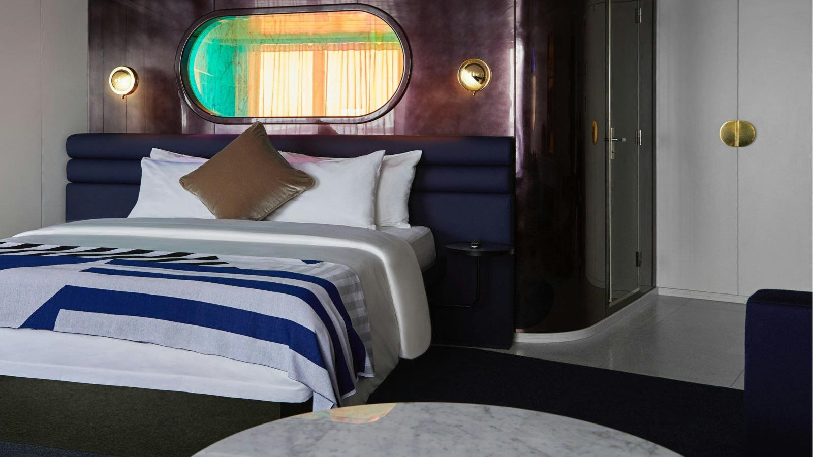 Official Virgin Voyages Gorgeous Suite master bedroom with oval peek-a-boo bathroom window